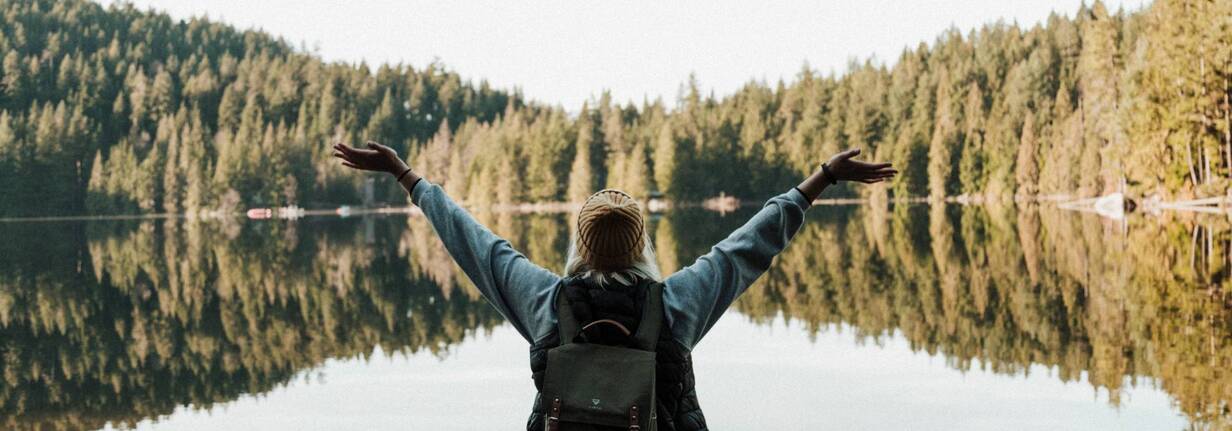 Digitalnomaden geniessen viele Freiheiten Eine junge Digitalnomadin steht vor einem See und freut sich.