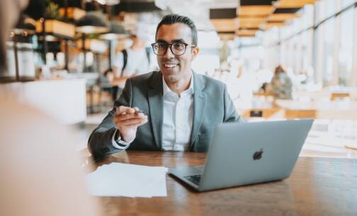 Mann mit MacBook im Café beim Gespräch