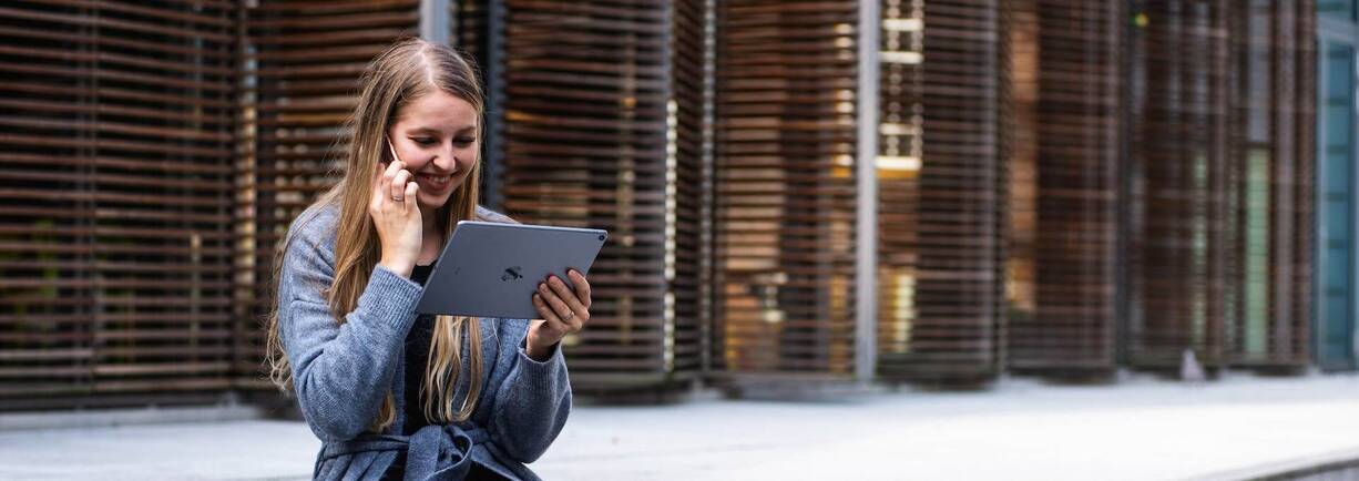 Frau mit iPad in der Hand und iPhone am Ohr