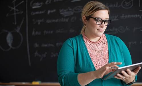 Lehrerin mit iPad vor einer schwarzen Tafel