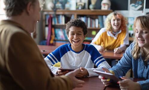 Lehrer hält iPad und lacht mit Lernenden