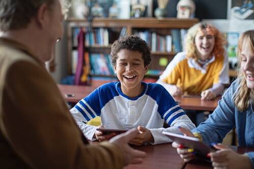 Lehrer hält iPad und lacht mit Lernenden