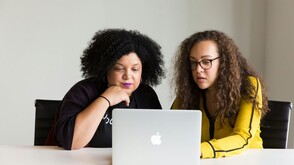 Zwei Frauen sitzen vor einem MacBook