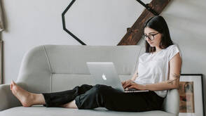 Eine junge Frau sitzt mit ihrem über MDM verwalteten Mac auf dem Sofa und arbeitet im Homeoffice 