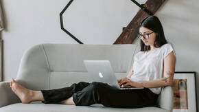 Eine junge Frau sitzt mit ihrem über MDM verwalteten Mac auf dem Sofa und arbeitet im Homeoffice 