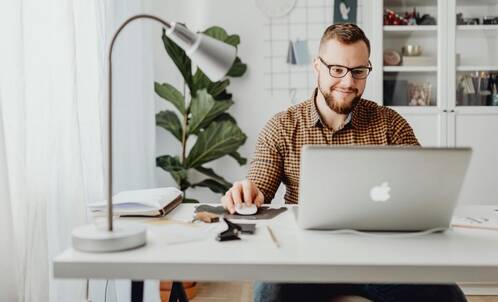 Ein Mann mit Brille sitzt an einem Pult mit seinem MacBook und schaut konzentriert auf das Display.
