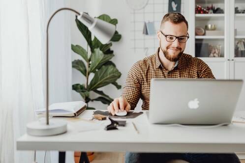 Ein Mann mit Brille sitzt an einem Pult mit seinem MacBook und schaut konzentriert auf das Display.