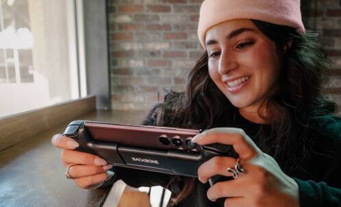 Eine junge Frau mit Beenie spielt auf dem iPhone ein Game