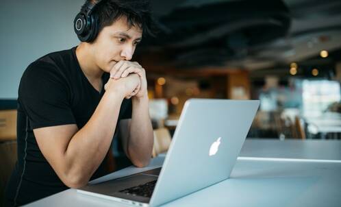 Mann sitzt mit Kopfhörer vor seinem MacBook