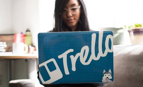 Eine junge Frau sitzt hinter ihrem Mac mit Trello-Sticker