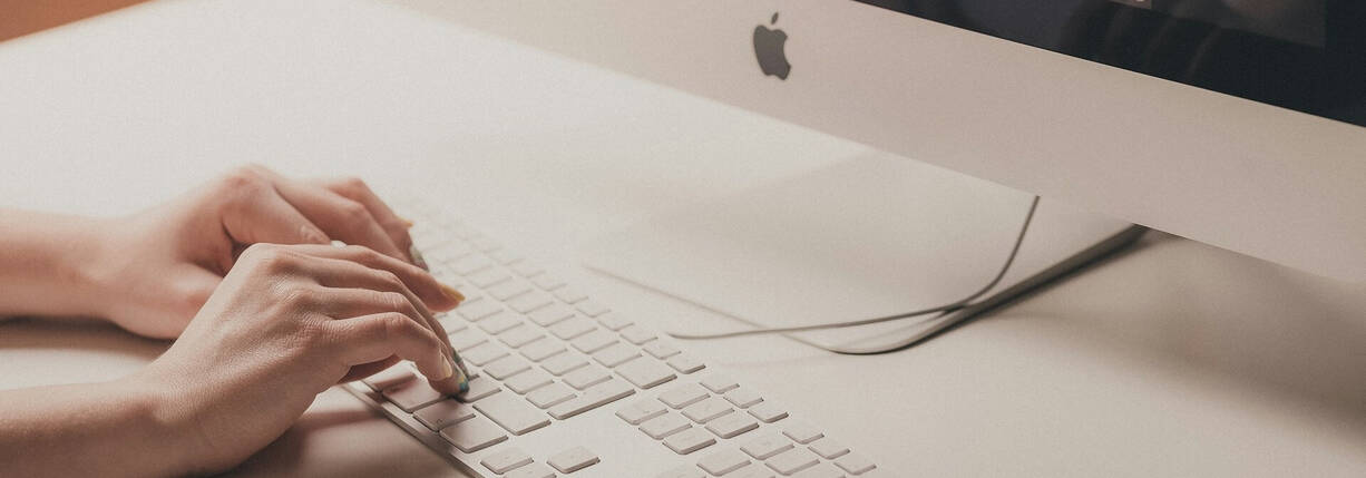 Zwei Hände schreiben auf Tastatur vor iMac