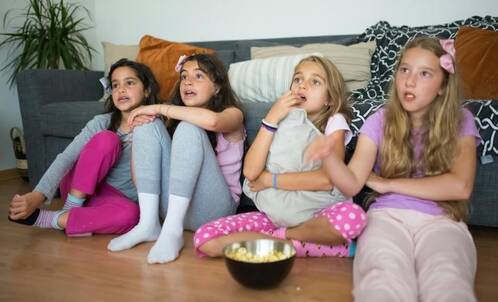 vier Mädchen sitzen mit Popcorn vor Bildschirm