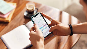 Hände halten iPhone mit Finanzen-App