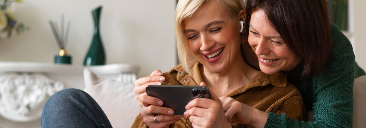 Zwei Frauen schauen lachend aufs iPhone