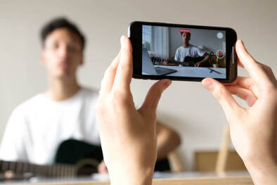 Junger Mann wird beim Gitarre Spielen mit iPhone gefilmt