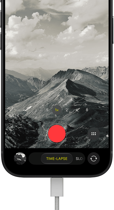 iPhone 18 Pro, Vorderseite, das Display zeigt eine Berglandschaft, mit der Kamera Modus Überlagerung im Zeitraffer Modus, mit dem Netzkabel am Ladeanschluss