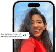 Ein iPhone 15 mit einer VoiceOver Beschreibung zu einem Foto: eine lachende Person mit welligem schwarzem Haar
