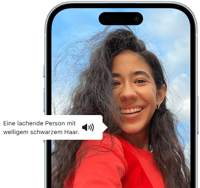 Ein iPhone 15 mit dem Feature VoiceOver, das eine Bildbeschreibung liefert: lachende Person mit welligem schwarzem Haar