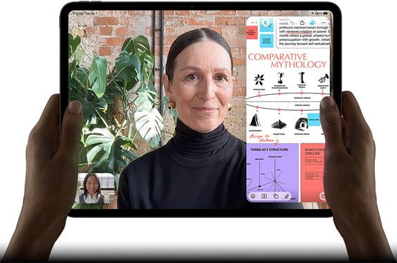 iPad Pro, Vorderansicht, Querformat, Farbe Space Schwarz, gerundete Ecken, schwarzer Displayrand, zwei Hände halten es an der linken und rechten Seite, das Display zeigt ein FaceTime Gespräch, das live übersetzt wird, und eine Lernapp zeigt eine Präsentation zum Thema „Vergleichende Mythologie“ mit Text, Diagrammen und handschriftlichen Notizen